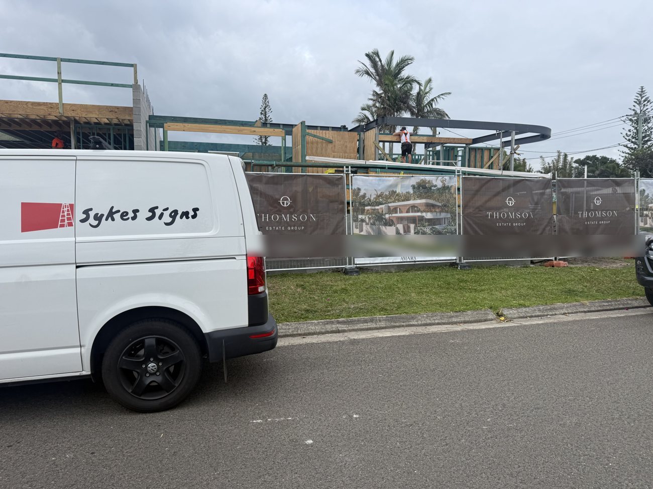 Sykes Signs van parked beside a row of printed mesh banners on temporary fencing along a street frontage in Marcoola