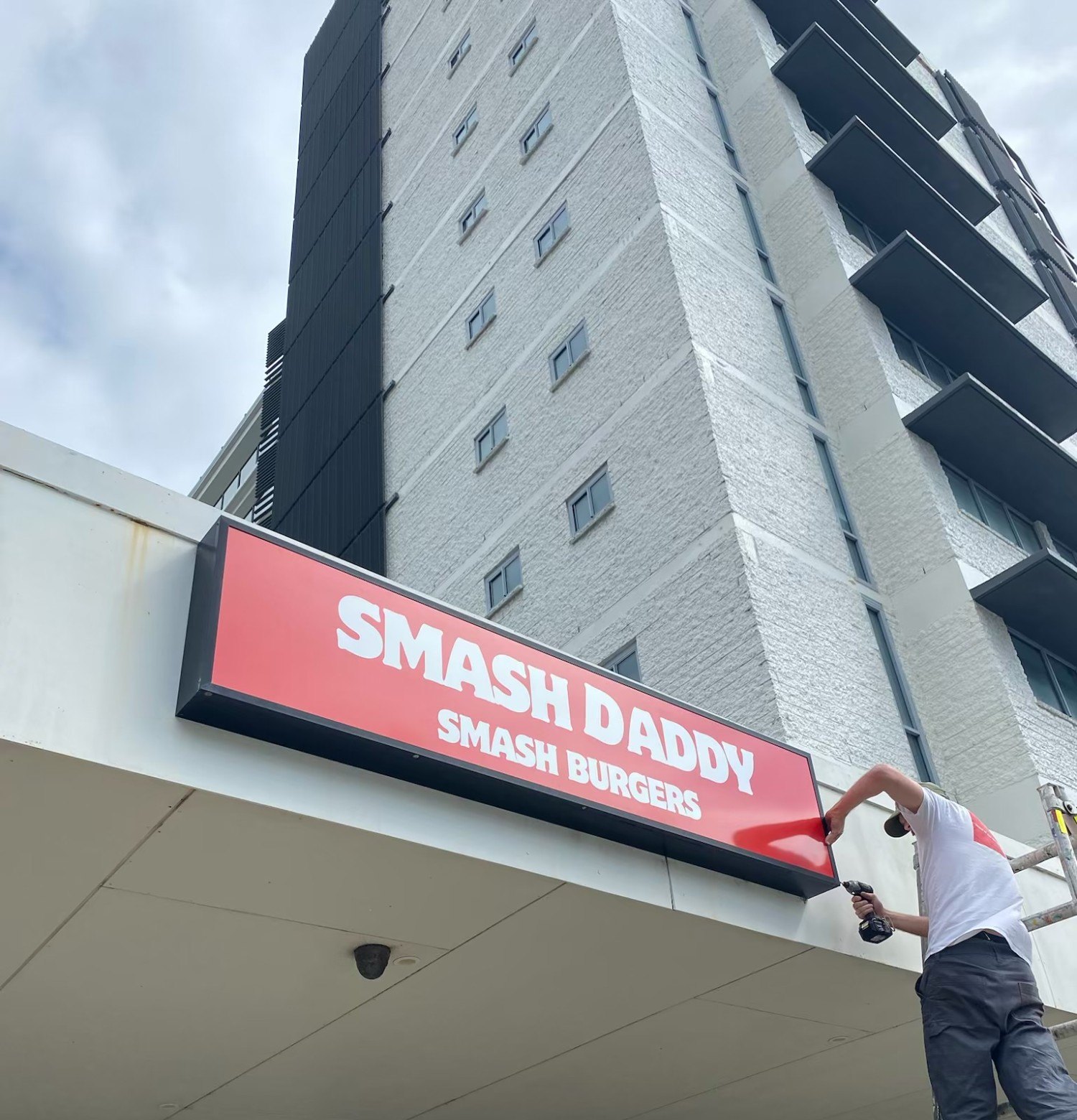 Red light box sign going up above the shopfront, low angle