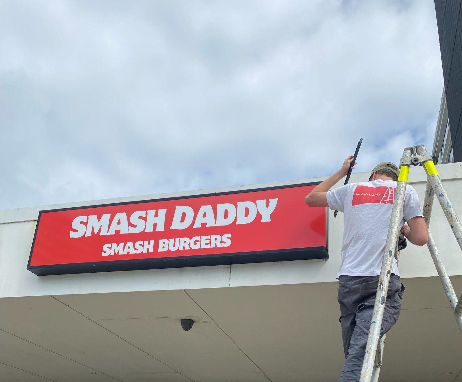 Sykes Signs installer on a scaffold fitting the red light box sign above the shopfront awning