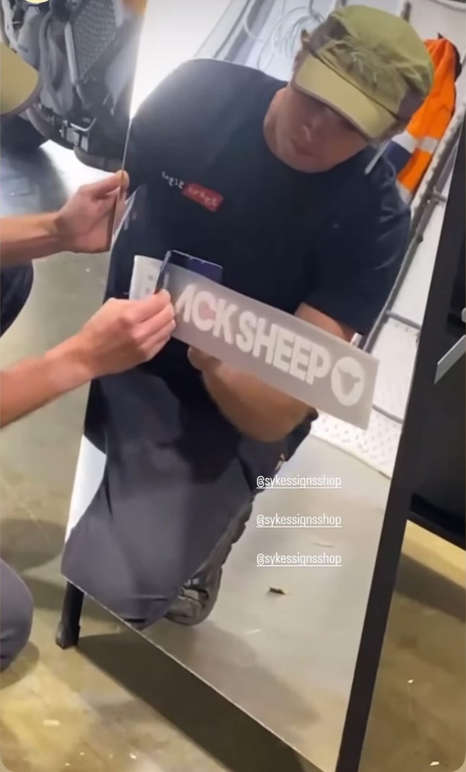 Applying Black Sheep logo vinyl to a mirror A-frame in the Sykes Signs workshop, Coolum Beach